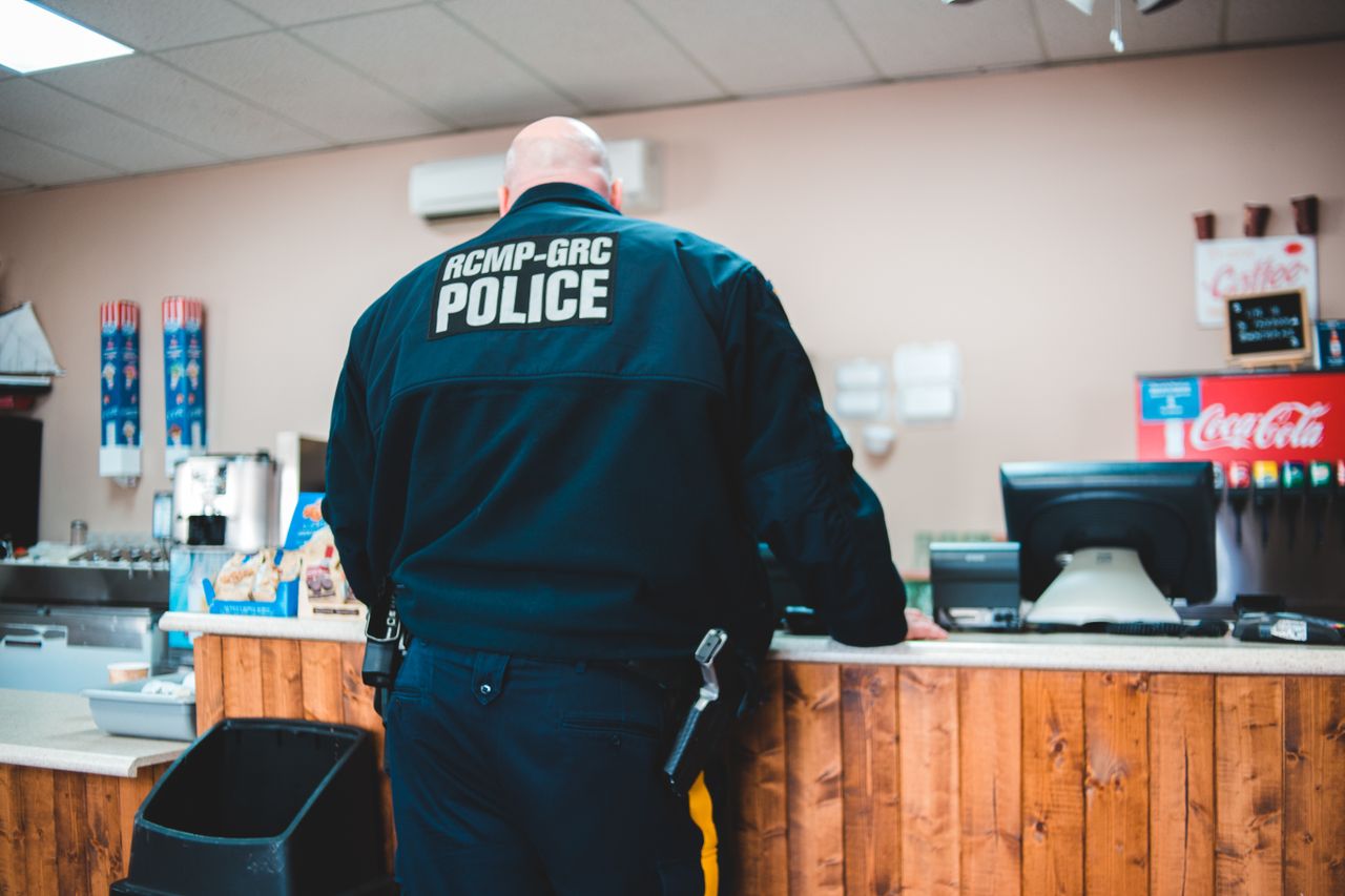 Services A police officer standing at a café counter ordering coffee, back view.