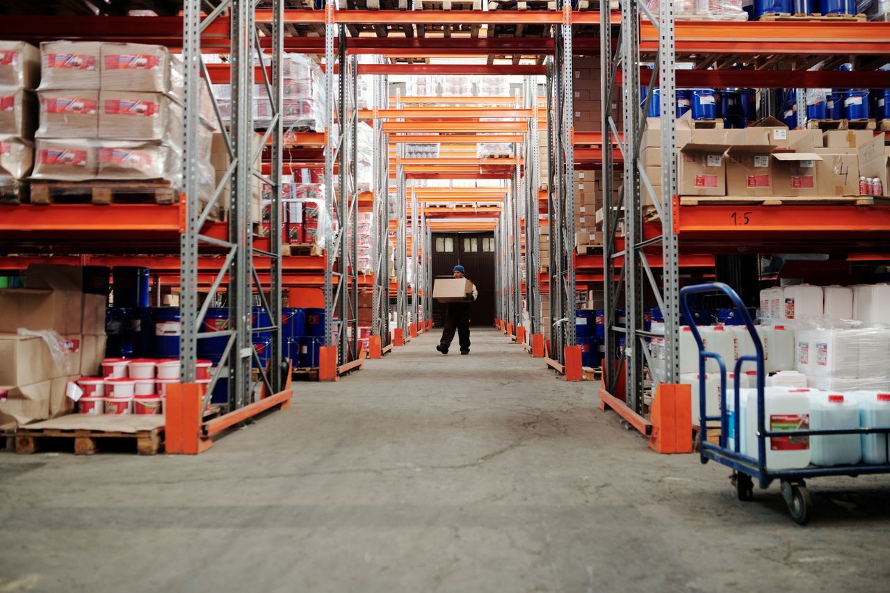 About A worker carrying a box in a well-organized warehouse storage aisle.